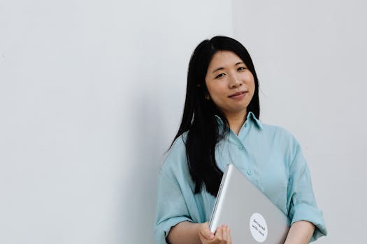 Asian woman smiling while holding a laptop against a white background.
