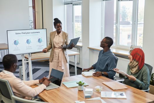 Diverse team engaged in a business presentation with charts on the screen in a modern office setting.