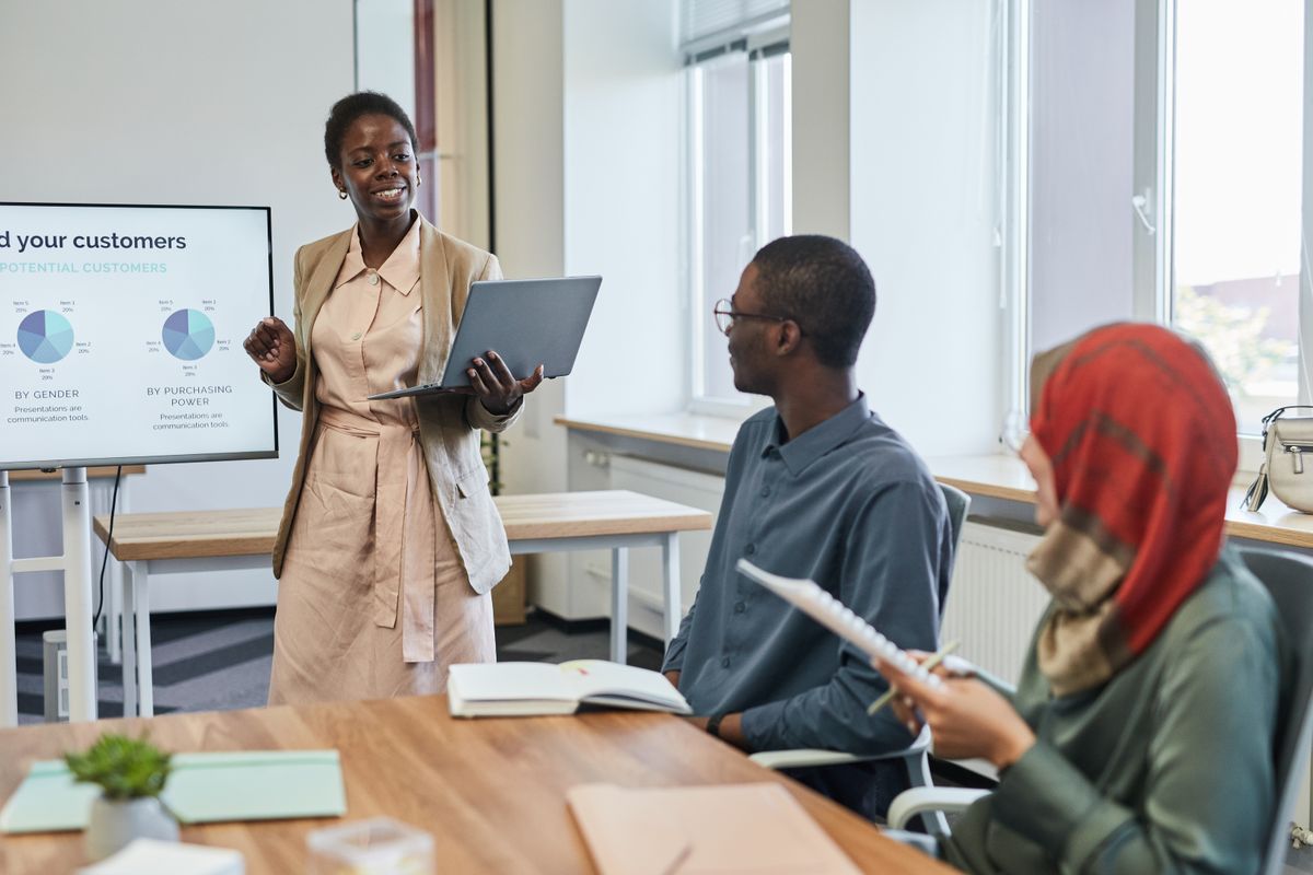 A woman delivering a presentation with charts on a large screen to her team
