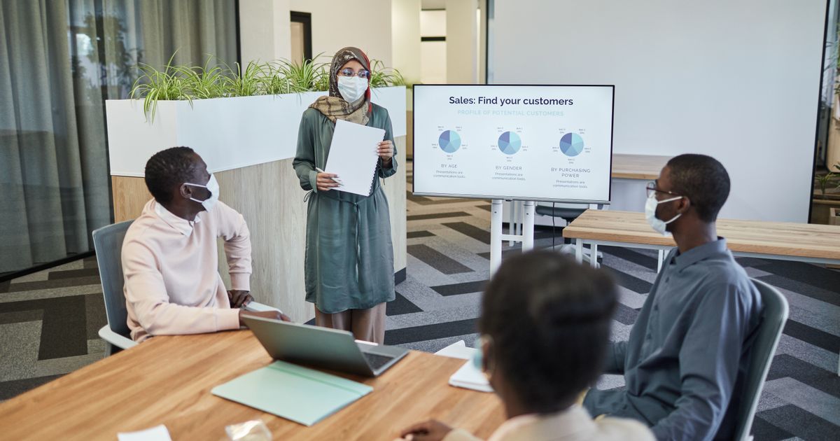 Colleagues wearing masks in a modern office discussing sales strategies.
