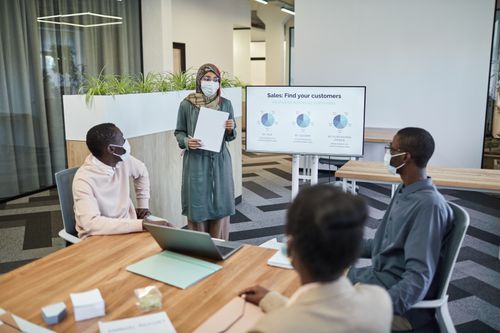 Free Colleagues wearing masks in a modern office discussing sales strategies. Stock Photo