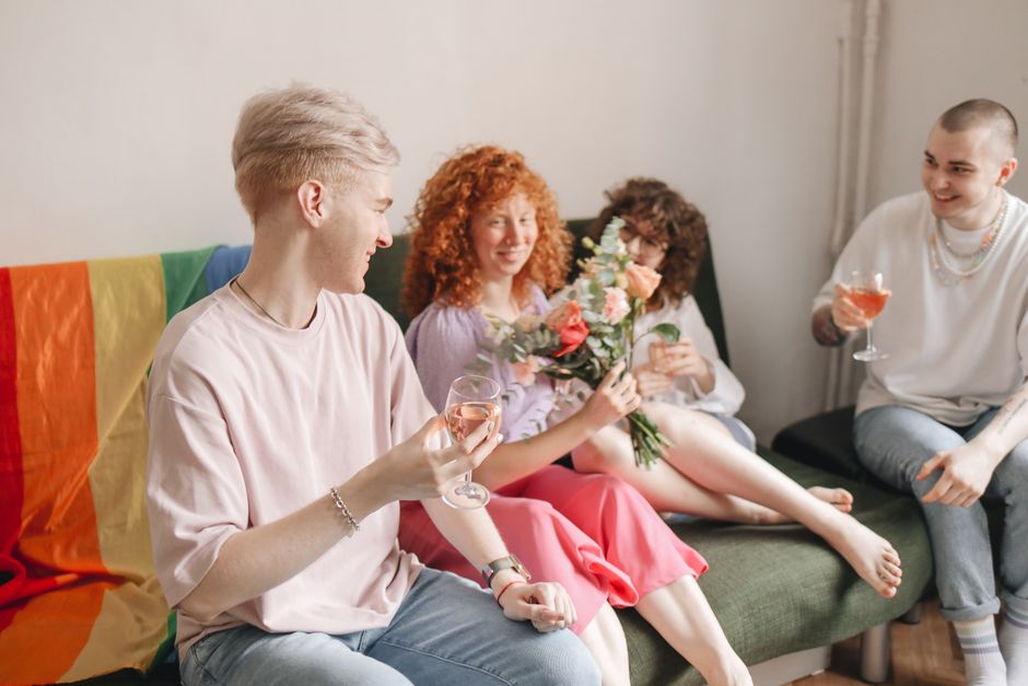 Group of friends celebrating indoors with drinks and flowers, laughing together.