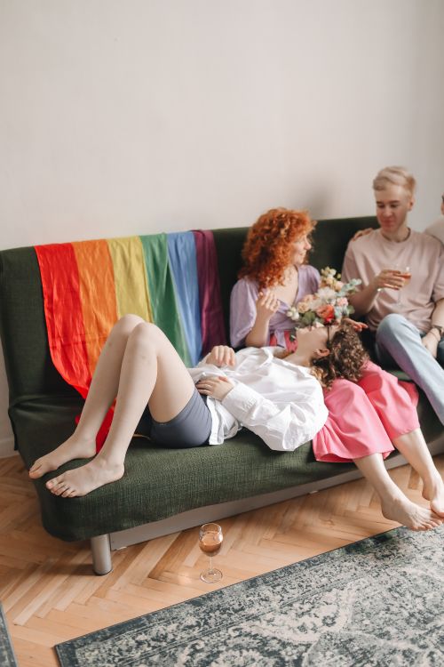 Free Three friends relaxing on a sofa with a rainbow flag, embodying a joyful and inclusive atmosphere. Stock Photo