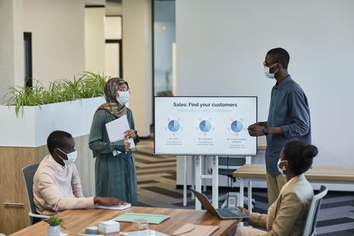 Free Business professionals in masks discuss customer profiles in a modern office setting. Stock Photo