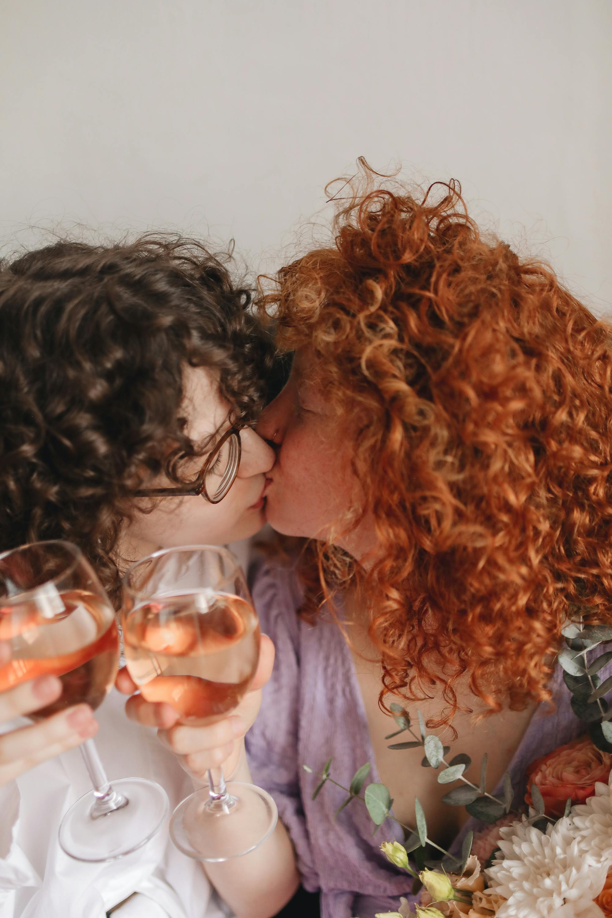 A tender kiss between two women sharing wine, showcasing love and togetherness.