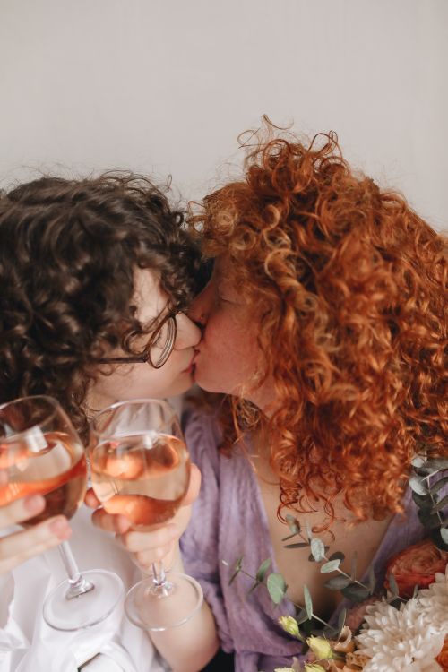 Free A tender kiss between two women sharing wine, showcasing love and togetherness. Stock Photo