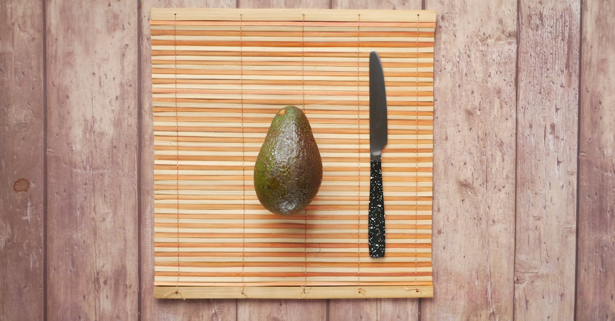 Top view of a fresh avocado and knife on a bamboo mat, perfect for food photography.
