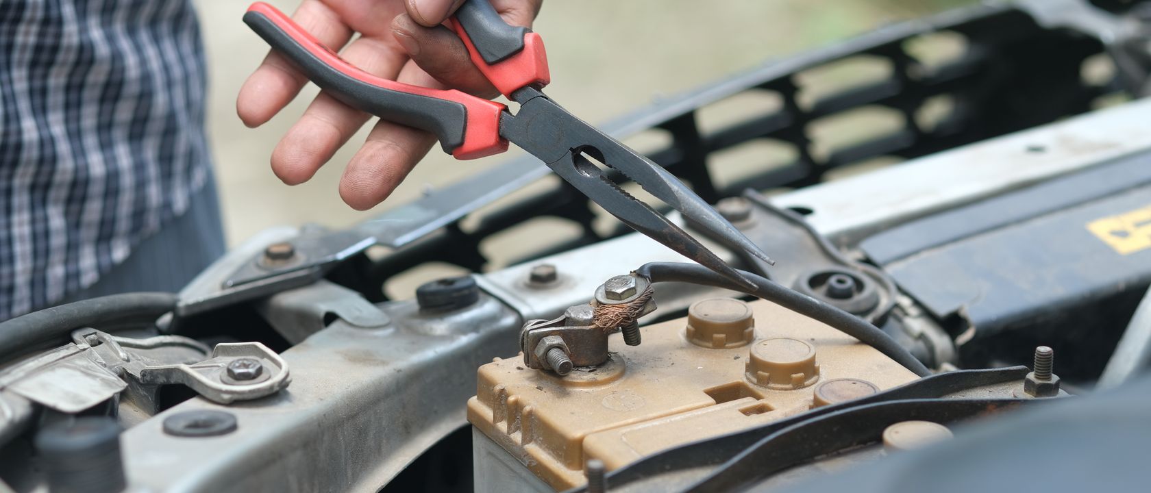 Person using pliers to check a car battery in an outdoor setting.