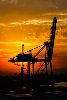 Silhouette of harbour cranes against a vibrant sunset sky at a cargo port.