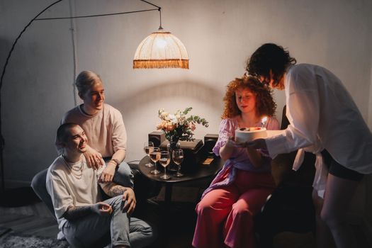 A small group of friends enjoying a cozy indoor birthday celebration with cake and drinks.