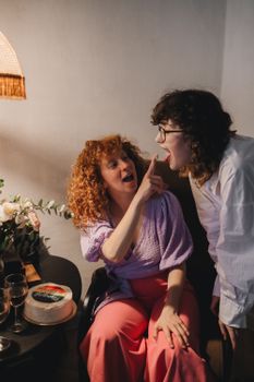 Two happy women celebrating with cake and laughter in a cozy indoor setting.