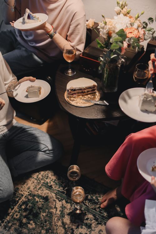 Free A warm indoor gathering with friends enjoying cake and drinks around a table. Stock Photo