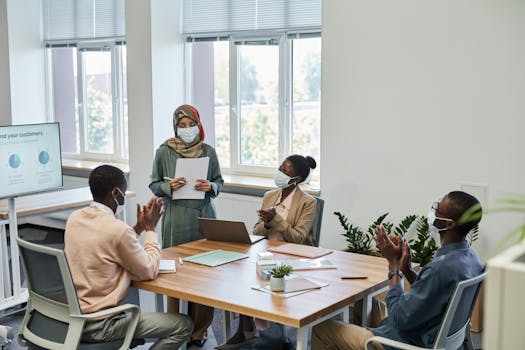 Diverse team collaborates in a modern office, focused on a presentation with social distancing measures.