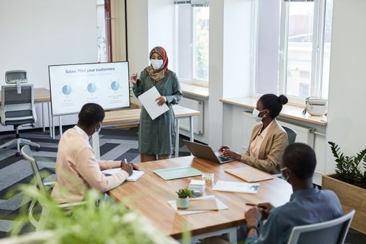 Business professionals in a COVID-safe office meeting, discussing sales strategies.