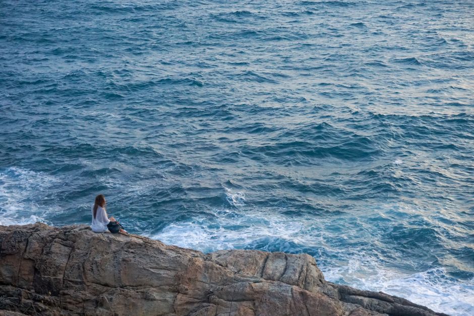 Mujer sentada sola sobre unas rocas contemplando el océano