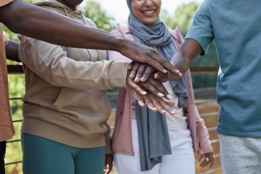A diverse group of friends stacking hands in a symbol of unity outdoors.