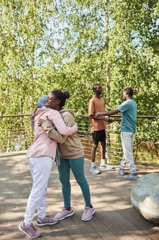 A joyful group of friends hugging and chatting outdoors in a sunny park setting, enjoying the summer weather.