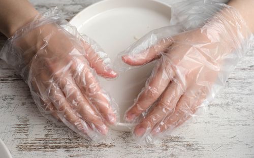 Free Close-up of hands in plastic gloves holding a plate on a wooden surface. Stock Photo