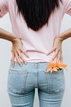 Back view of a woman in jeans with flowers tucked into the pocket. Casual style.