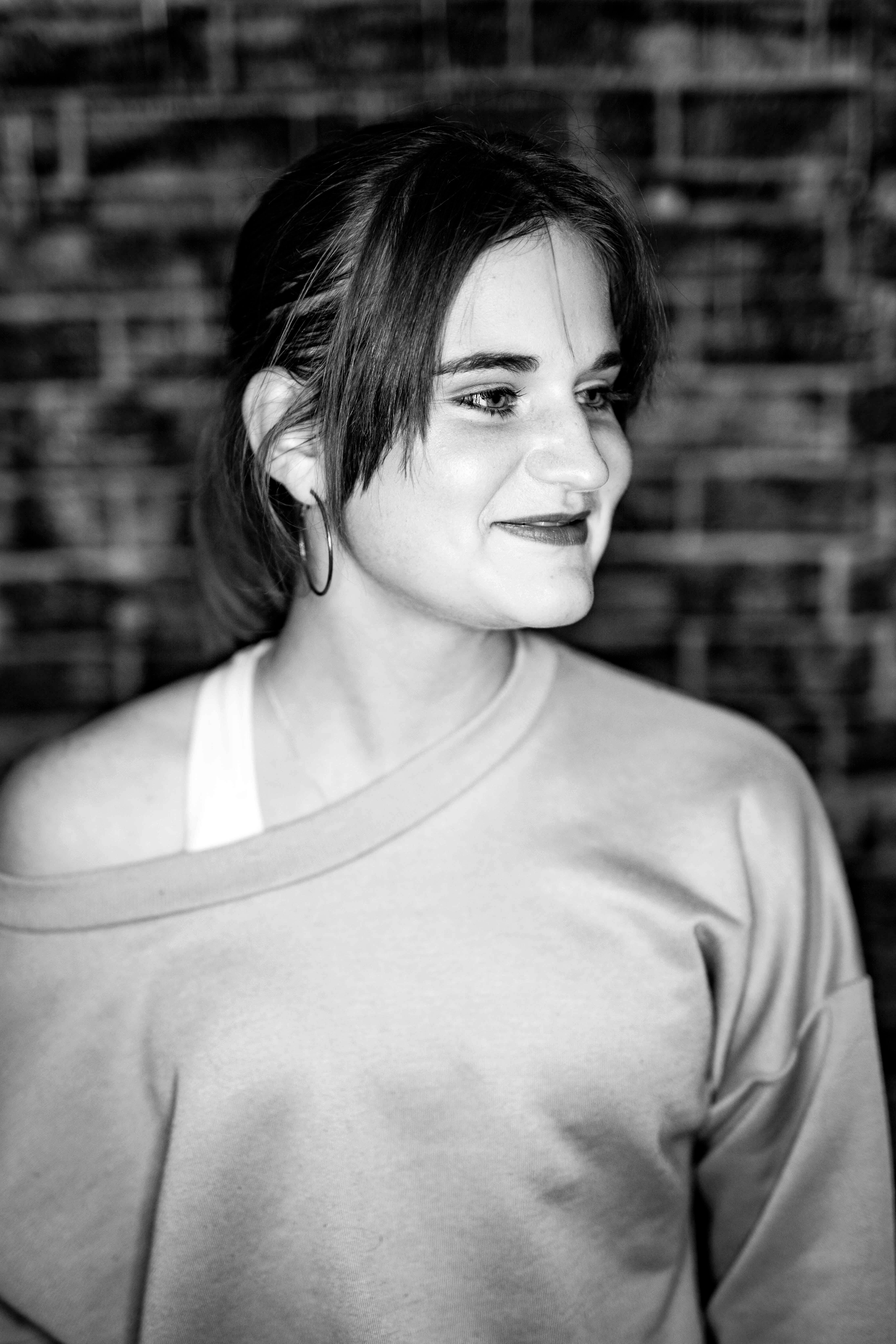 Grayscale portrait of a smiling woman looking sideways against a brick wall.