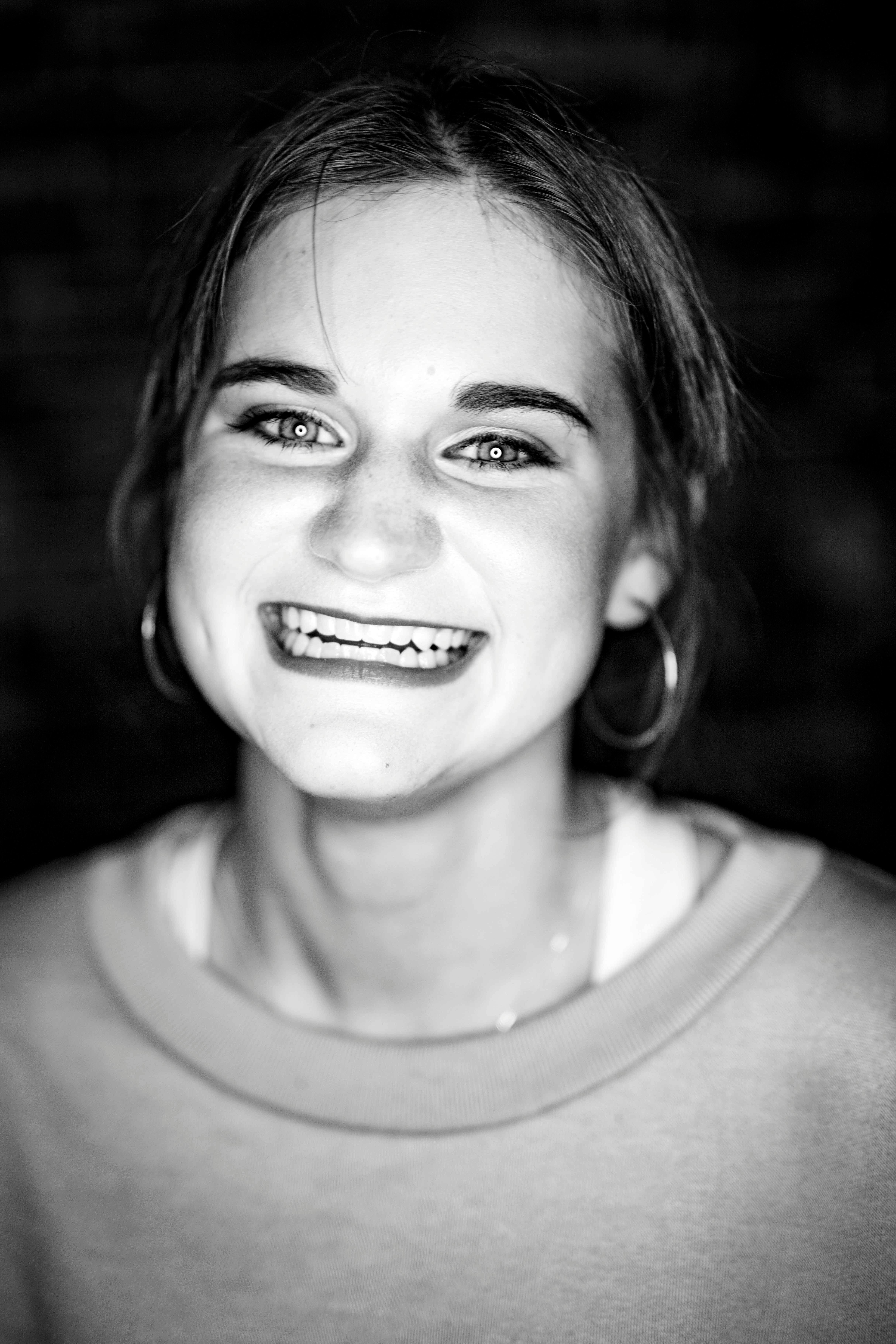 Close-up monochrome portrait of a smiling woman with hoop earrings, exuding happiness.