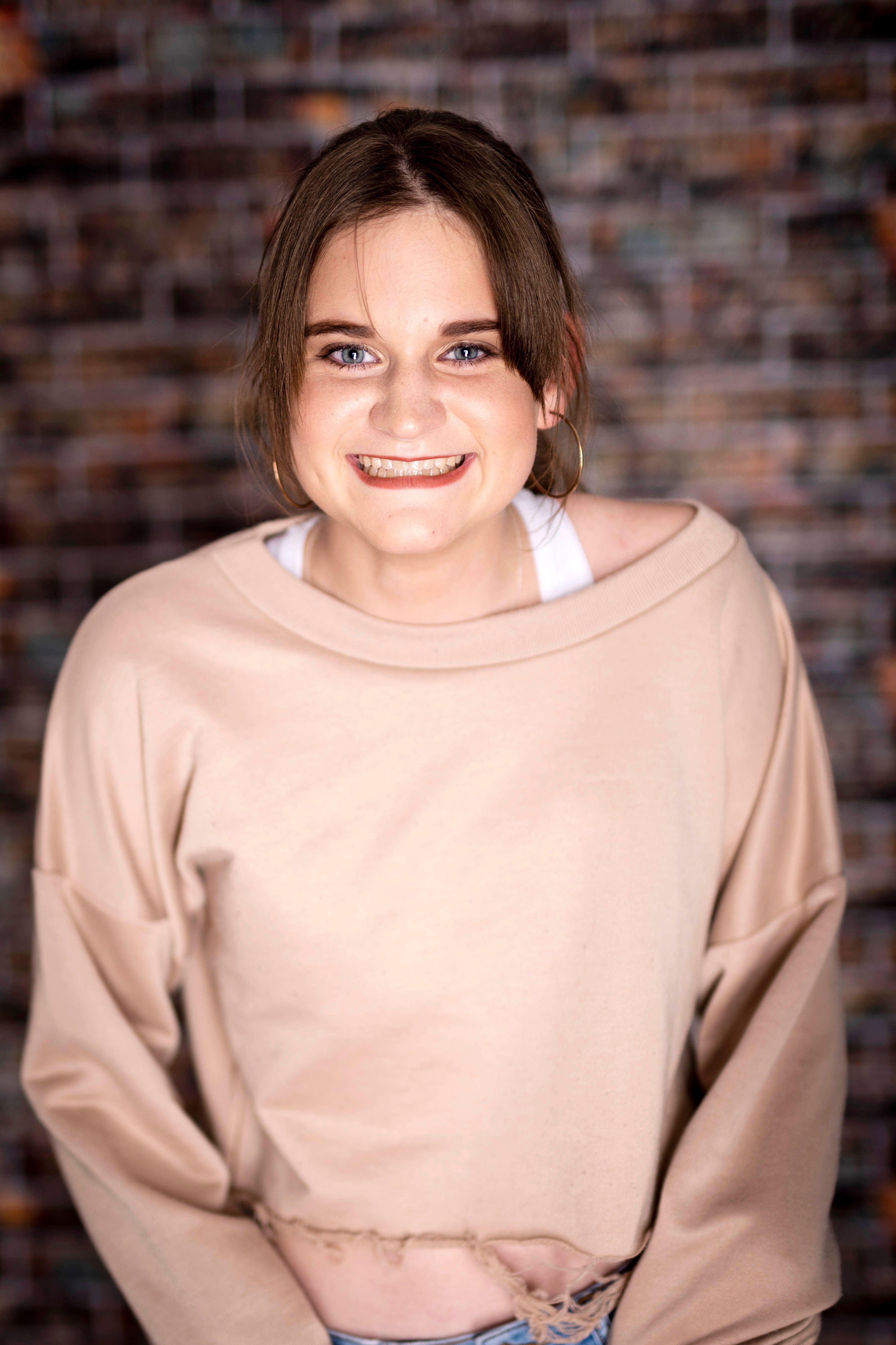 Portrait of a cheerful teen girl smiling in a casual beige sweater against a textured background.