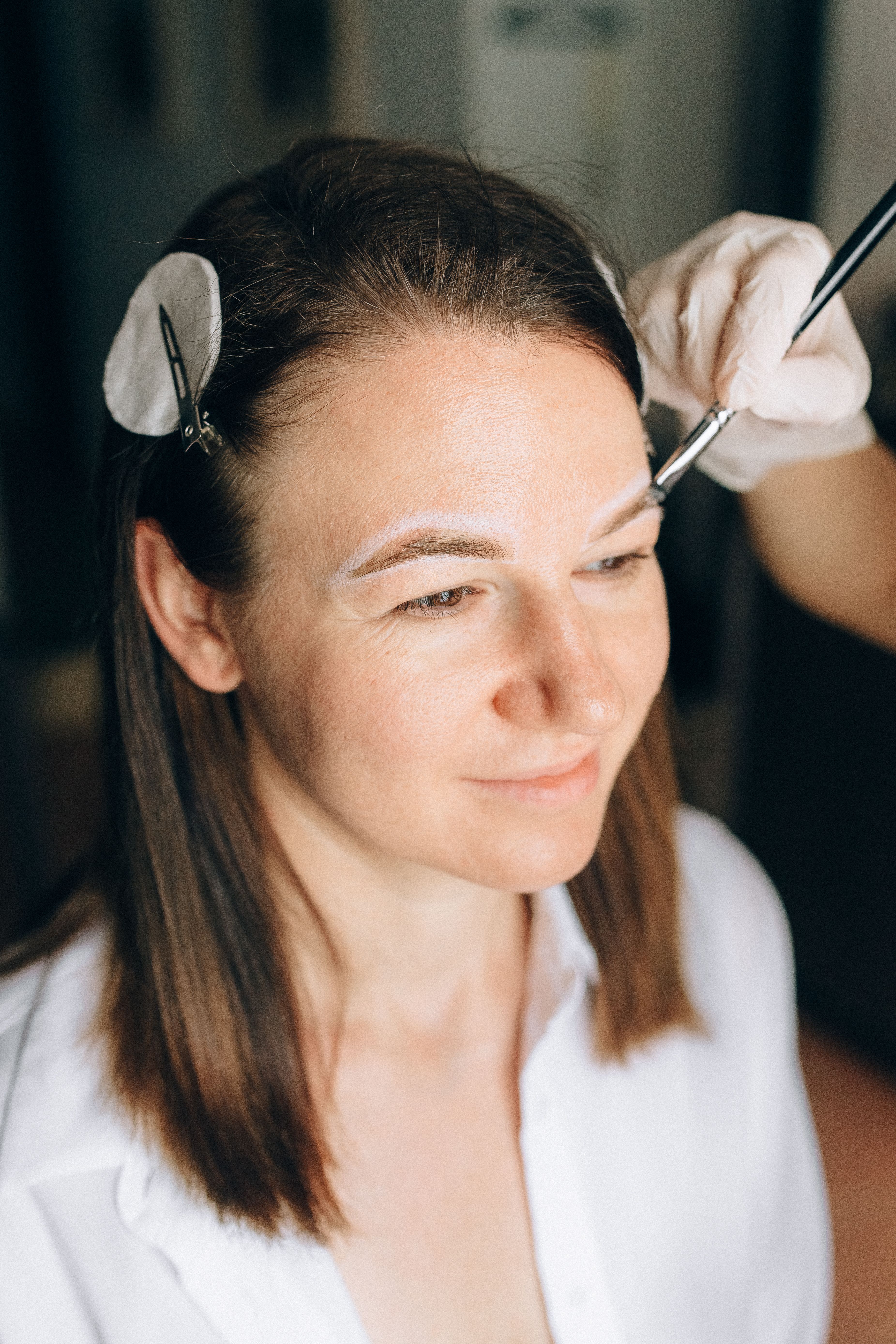 Woman undergoing eyebrow contouring with a makeup brush in a salon setting.