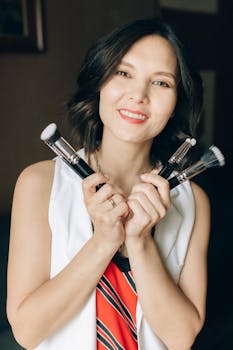 Smiling woman with short hair holding makeup brushes indoors, perfect for cosmetology and beauty themes.