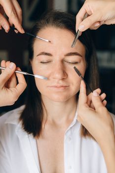 Close-up of a woman with eyes closed receiving makeup using various brushes and tools.