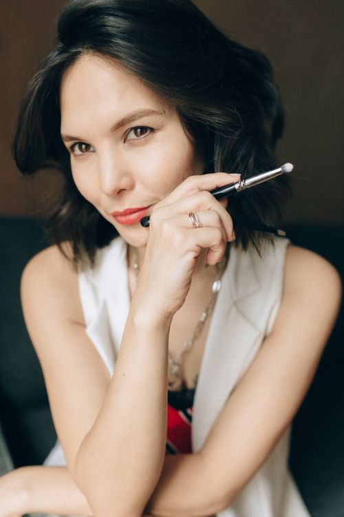 Free Portrait of a stylish woman with a makeup brush indoors, exuding confidence and elegance. Stock Photo
