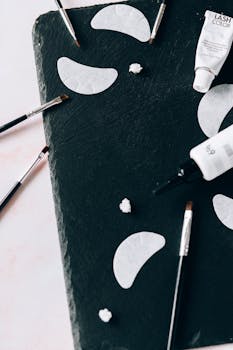 Artistic flat lay of makeup tools and cosmetics on a dark slate surface.