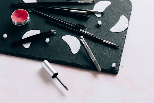 Aesthetic arrangement of various makeup tools like brushes and tweezers on a black slate surface.