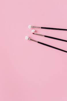 Three makeup brushes on a pastel pink surface, perfect for beauty and cosmetic themes.