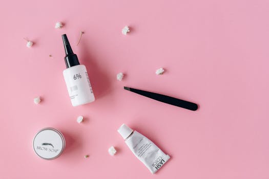 Cosmetic products and tools on a pink background with delicate flowers.