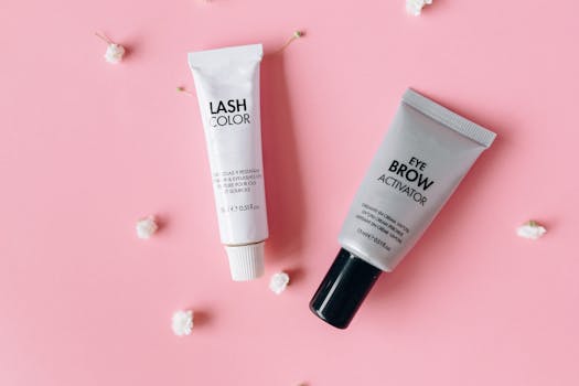 Flat lay of lash color and eyebrow activator tubes on a pink surface.