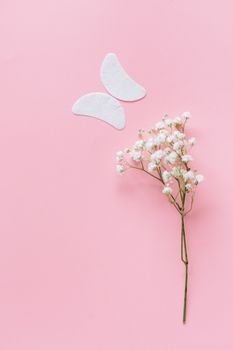 Minimalist composition of baby's breath and under-eye patches on a pink backdrop.