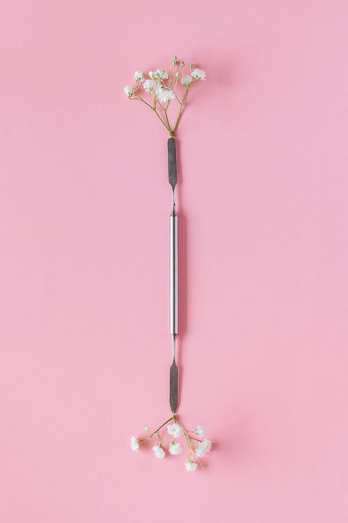 Stainless Steel Cuticle Pusher with Flowers on Both Ends Lying on Pink Background