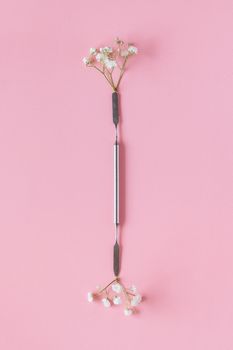 Elegant nail care tool paired with delicate flowers against a pastel pink background.