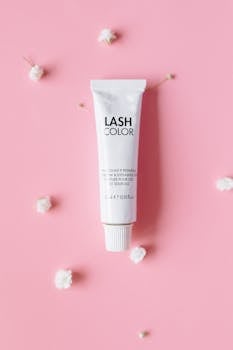Minimalist flat lay of a lash color tube with white flowers on a pink background.
