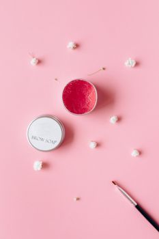 Flat lay of brow soap and brush on a pink surface with small white flowers.