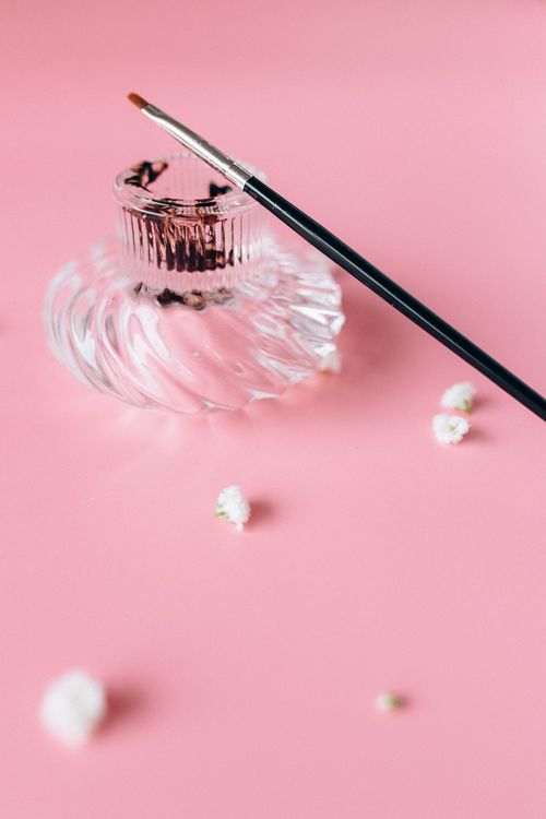 Free Stylish glass perfume bottle with a makeup brush on a pink backdrop, conveying elegance. Stock Photo