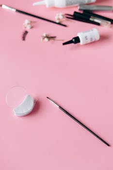 Close-up of makeup tools on a pink surface, featuring brushes and accessories.
