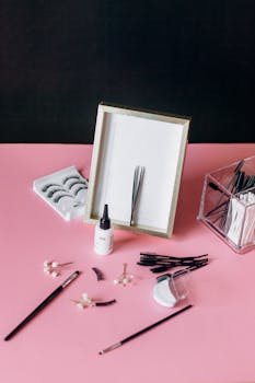 Aesthetic layout of beauty tools and accessories on a pink background with a framed artwork.