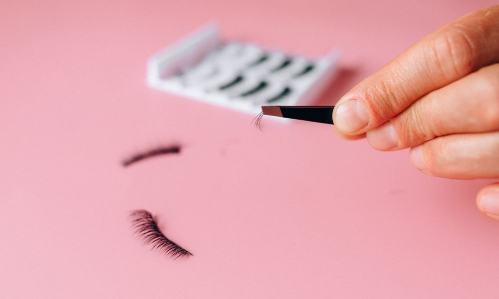 Applying lashes with tweezers over a pink background