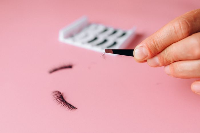 Lashes held in tweezers on a pink background