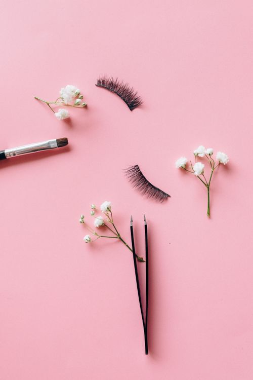 Free Chic flat lay of false eyelashes, flowers, and a makeup brush on a pink surface. Stock Photo