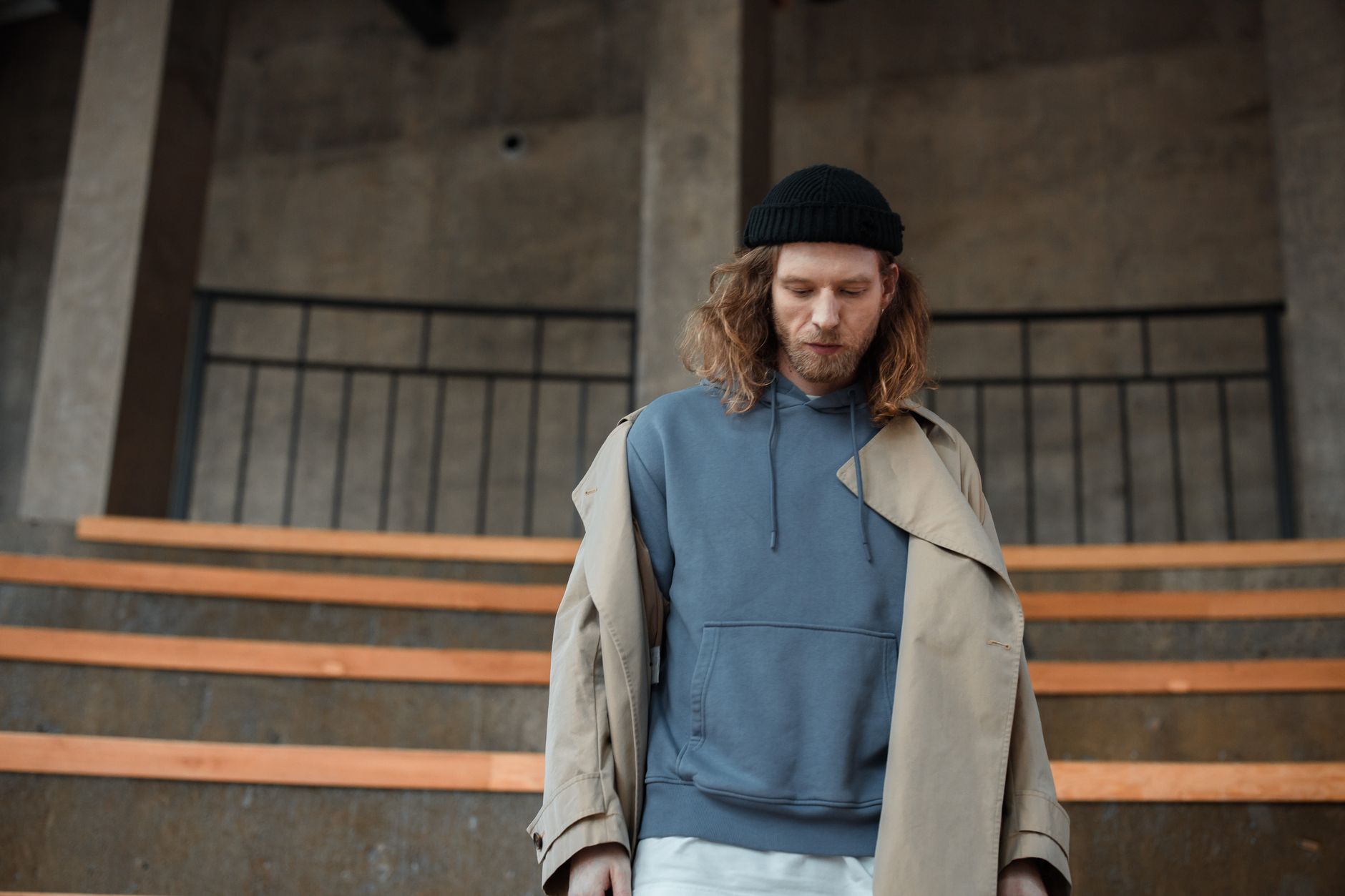 Homme en sweat à capuche et trench-coat dans un décor urbain streetwear premium