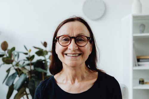 Free Portrait of a happy elderly woman wearing glasses, smiling in an indoor setting. Stock Photo