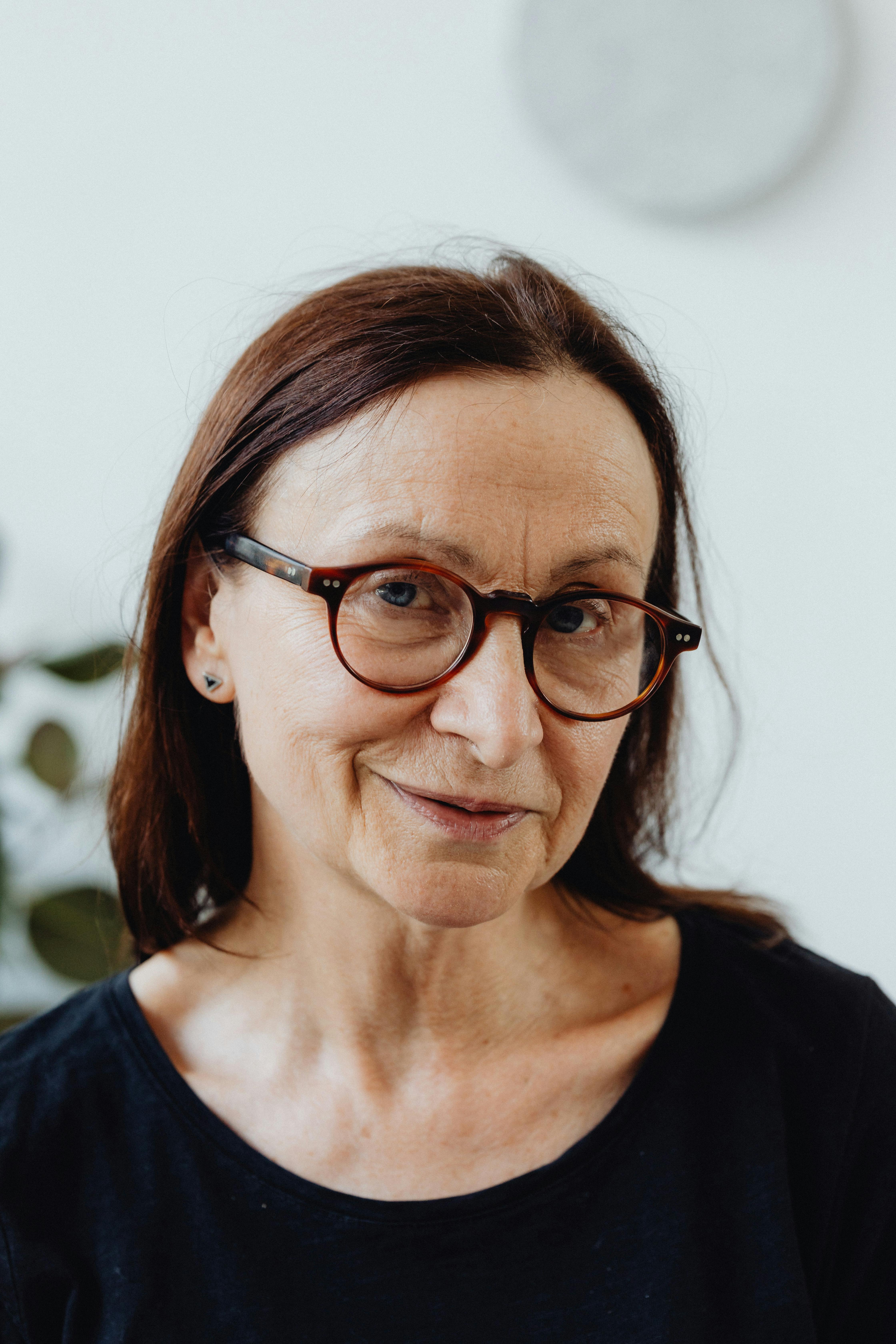 Portrait of a mature woman with eyeglasses smiling indoors. Bright and cheerful vibe.