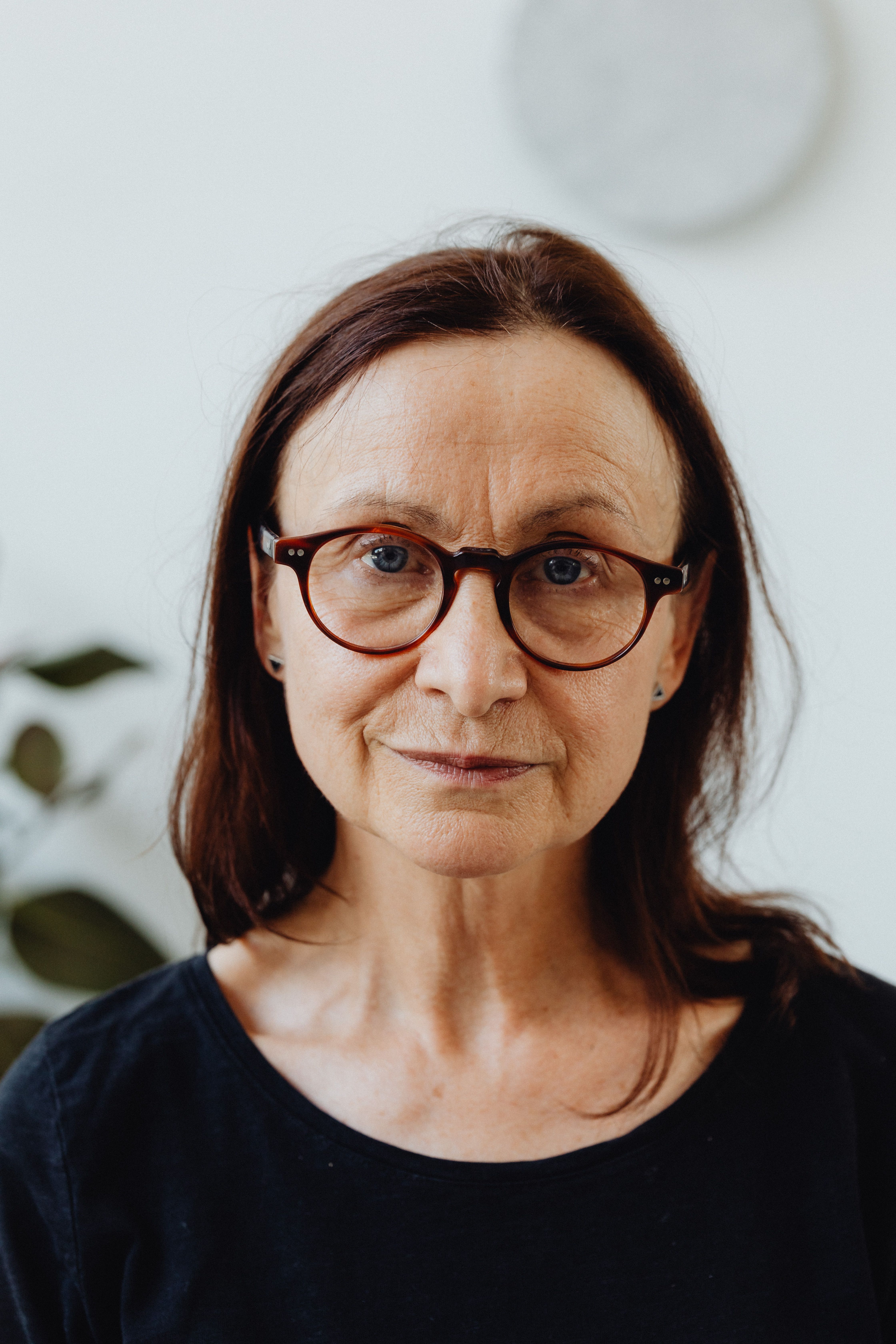 Portrait of an elderly woman wearing glasses and a black shirt, looking directly at the camera.